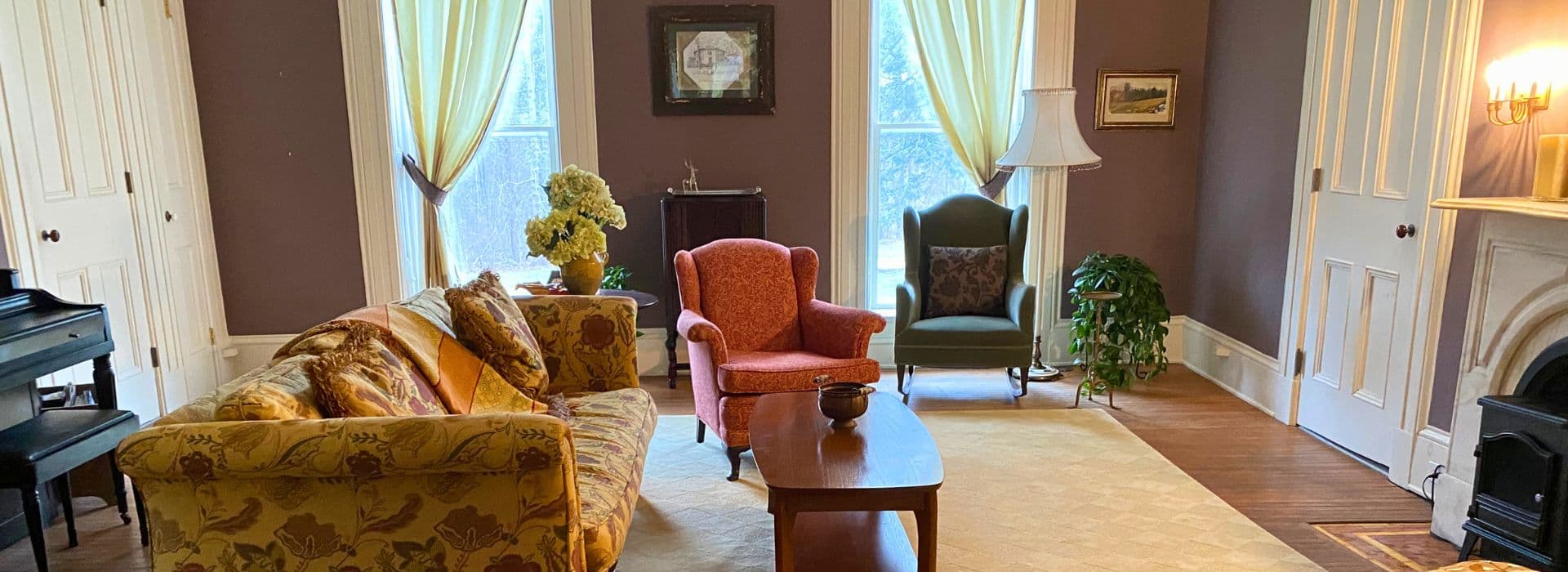 A cozy living room featuring colorful furniture, a coffee table, and large windows with sheer curtains.