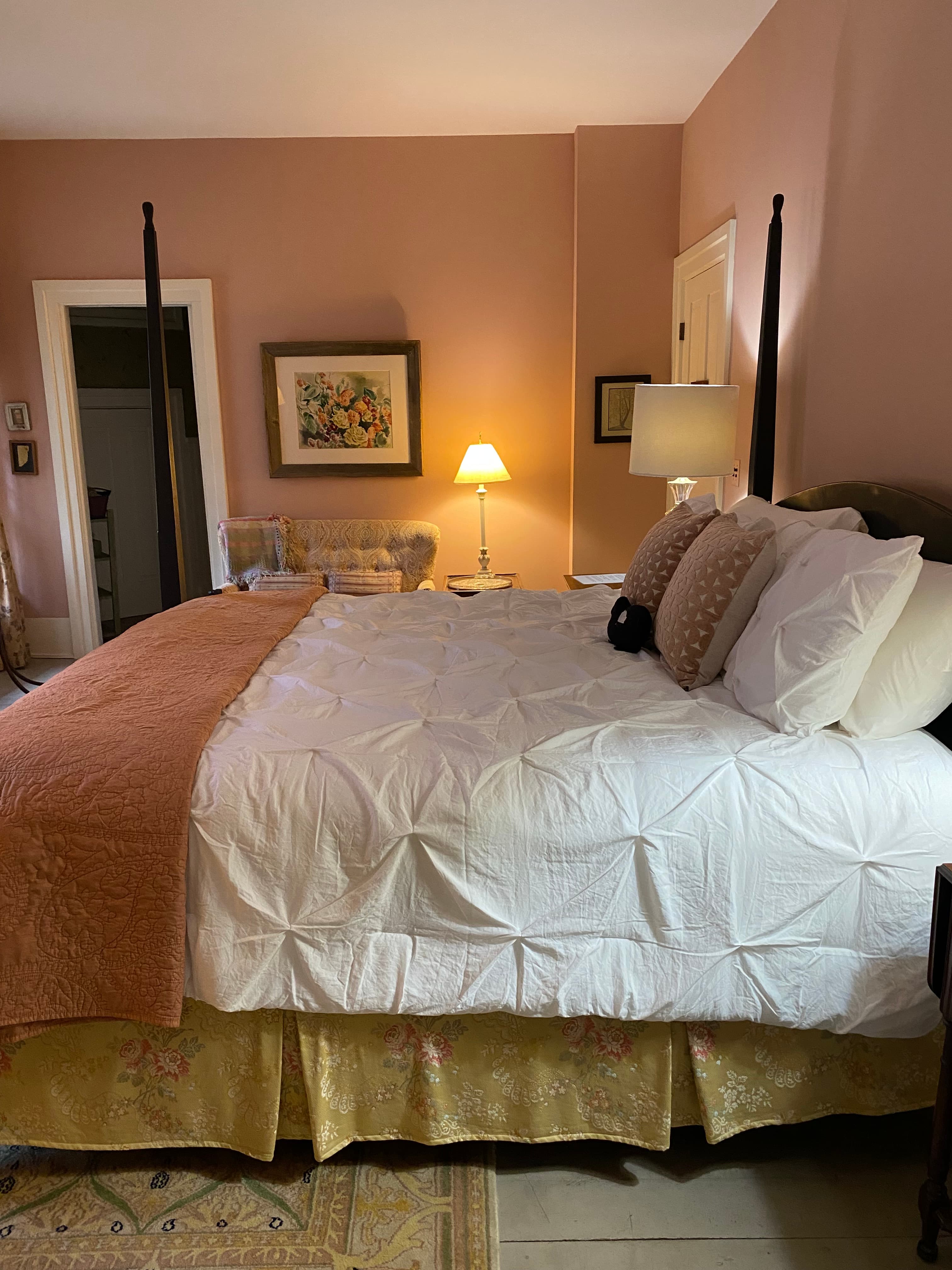 Cozy bedroom featuring a four-poster bed with a white quilt, an orange throw, and soft lighting.