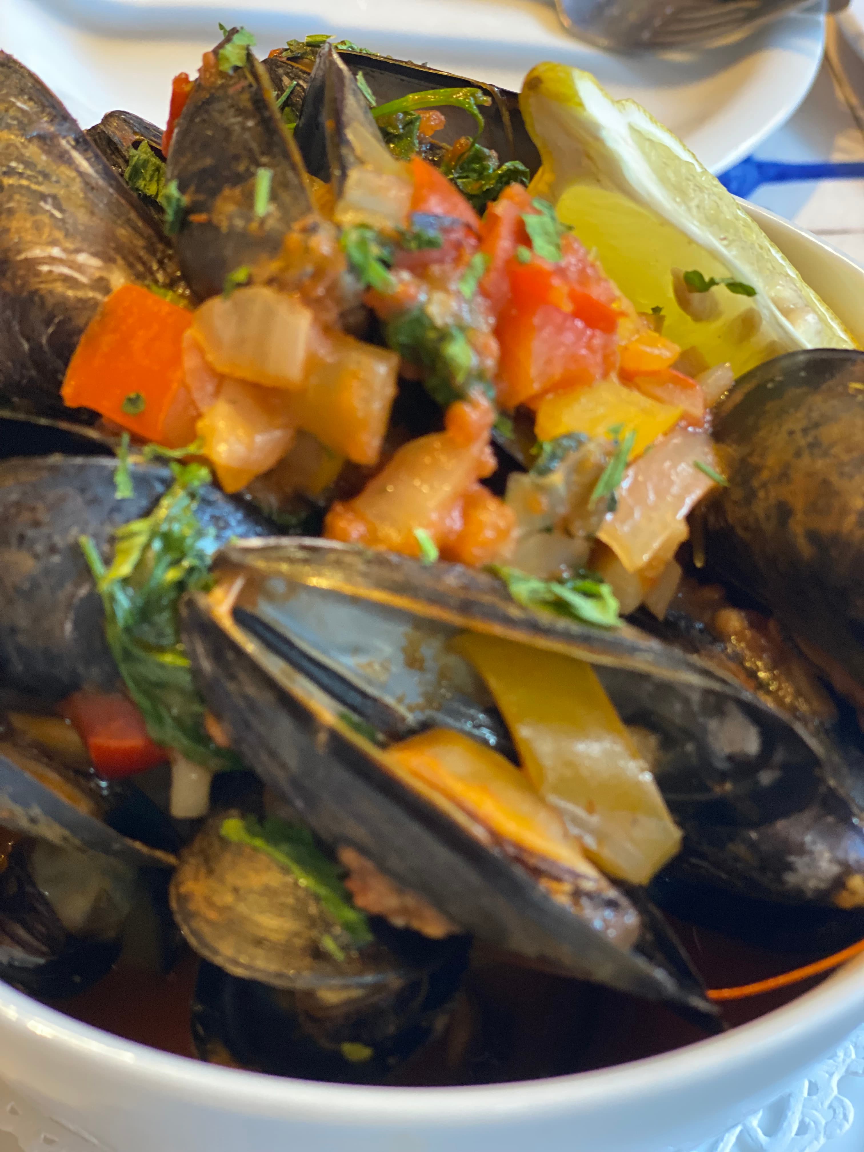 A bowl of mussels topped with a colorful medley of diced vegetables and a wedge of lime.