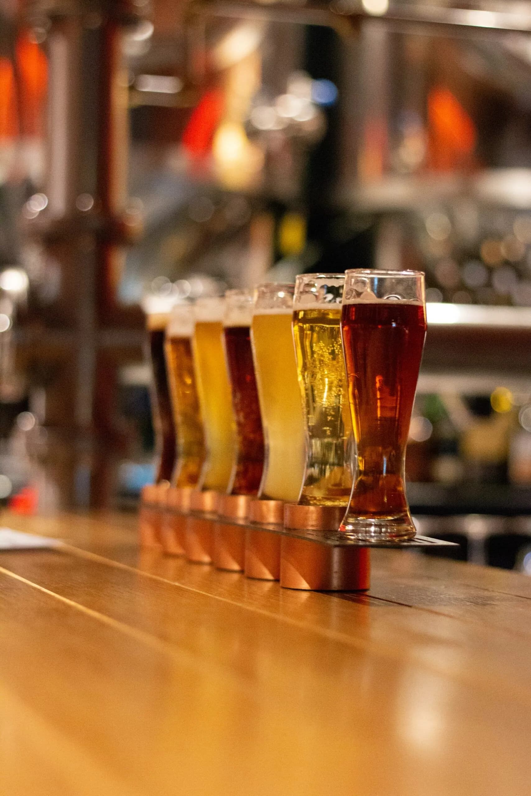 A row of six colorful beer glasses on a wooden bar.