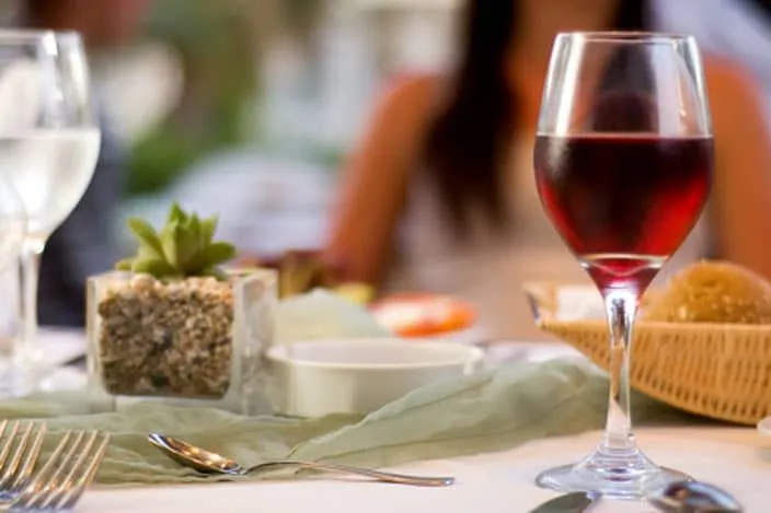 A glass of red wine sits on a dining table with a small succulent centerpiece and other dining elements in the background.