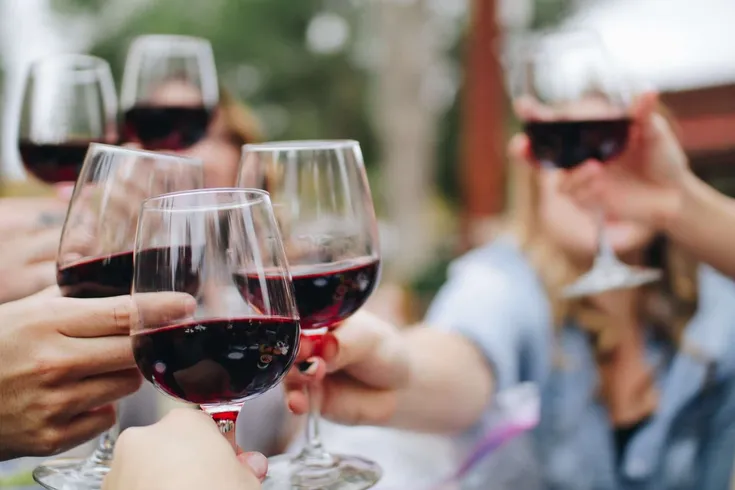 A group of hands clinking glasses filled with red wine.