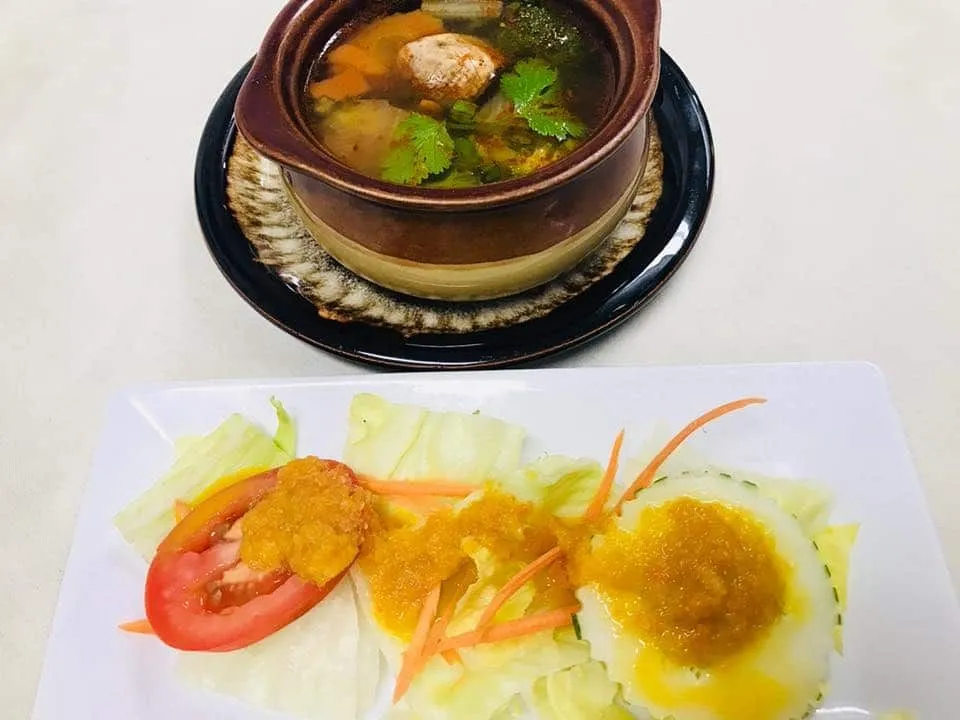 A plate of fresh salad with tomato, cucumber, and dressing, accompanied by a bowl of soup garnished with herbs.