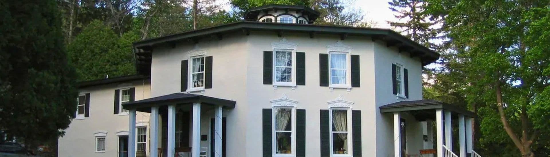 A large, octagonal house with green shutters and a porch surrounded by trees.